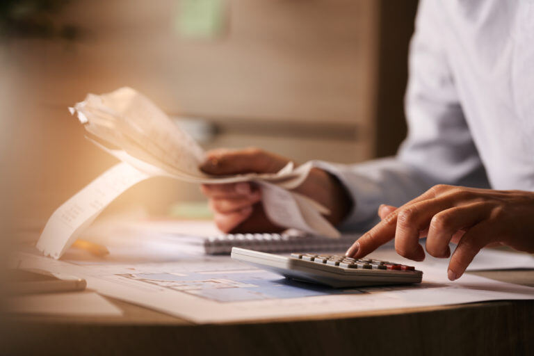 closeup-economist-using-calculator-while-going-through-bills-taxes-office-768x512