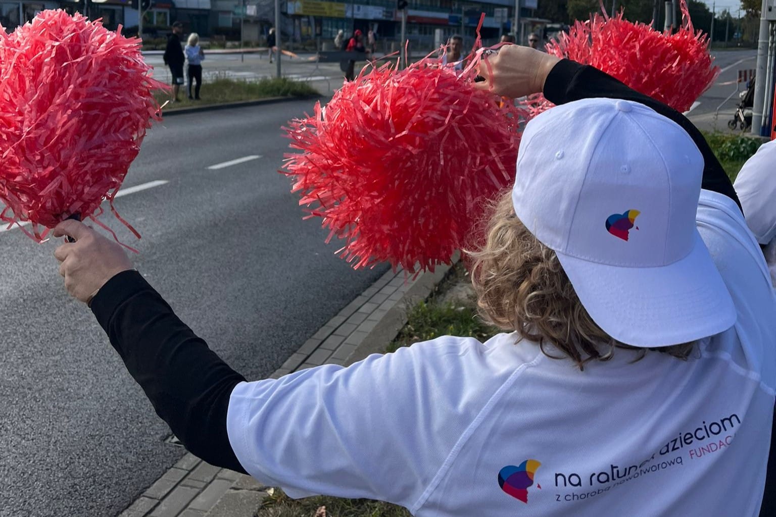 kobieta z pomponami do kibicowania, ujęcie od tyłu, na koszulce widoczne logo fundacji